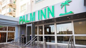 The exterior of a Palm Inn hotel with a prominent sign, large windows, and a staircase leading to the entrance. - Palm Inn Hotel (Hurghada)
