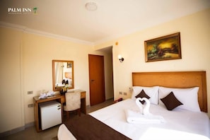 Une chambre d’hôtel avec un lit, un bureau, un petit réfrigérateur, un miroir et un tableau au mur.