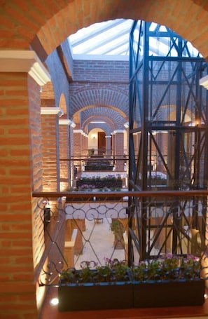 A brick interior with a glass ceiling, a metal staircase, and a flower box. - Hotel Otavalo (Otavalo)