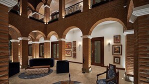 A lobby with brick arches, a sofa, a chair, and artwork on the walls. - Hotel Otavalo (Otavalo)
