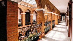 A corridor with brick arches, a skylight, and a metal railing with plants. - Hotel Otavalo (Otavalo)