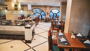 A restaurant with a marble floor, wooden tables, and chairs, and a view through arched windows. - Astoneast Taiba Hotel Ex Artal Al Alami  (Madinah)