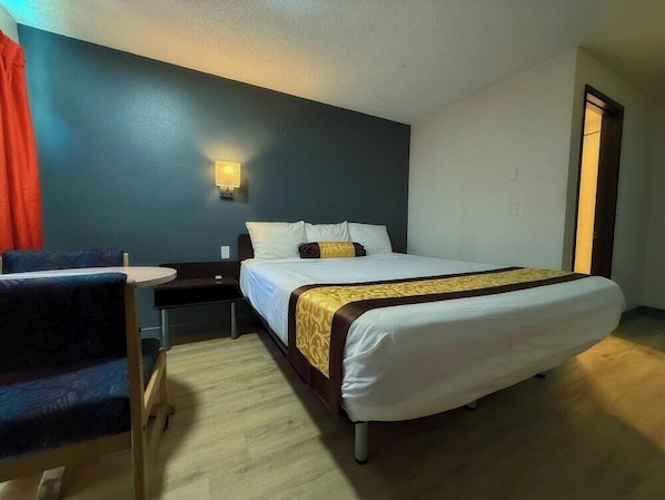 A hotel room with a bed, bedside table, chair, and a wall-mounted light. - OYO Hotel Hermiston OR Downtown (Hermiston)