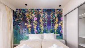 Ein Doppelbett mit weißer Bettwäsche, ein großes Blumenmural an der Wand und ein Kleiderschrank rechts.