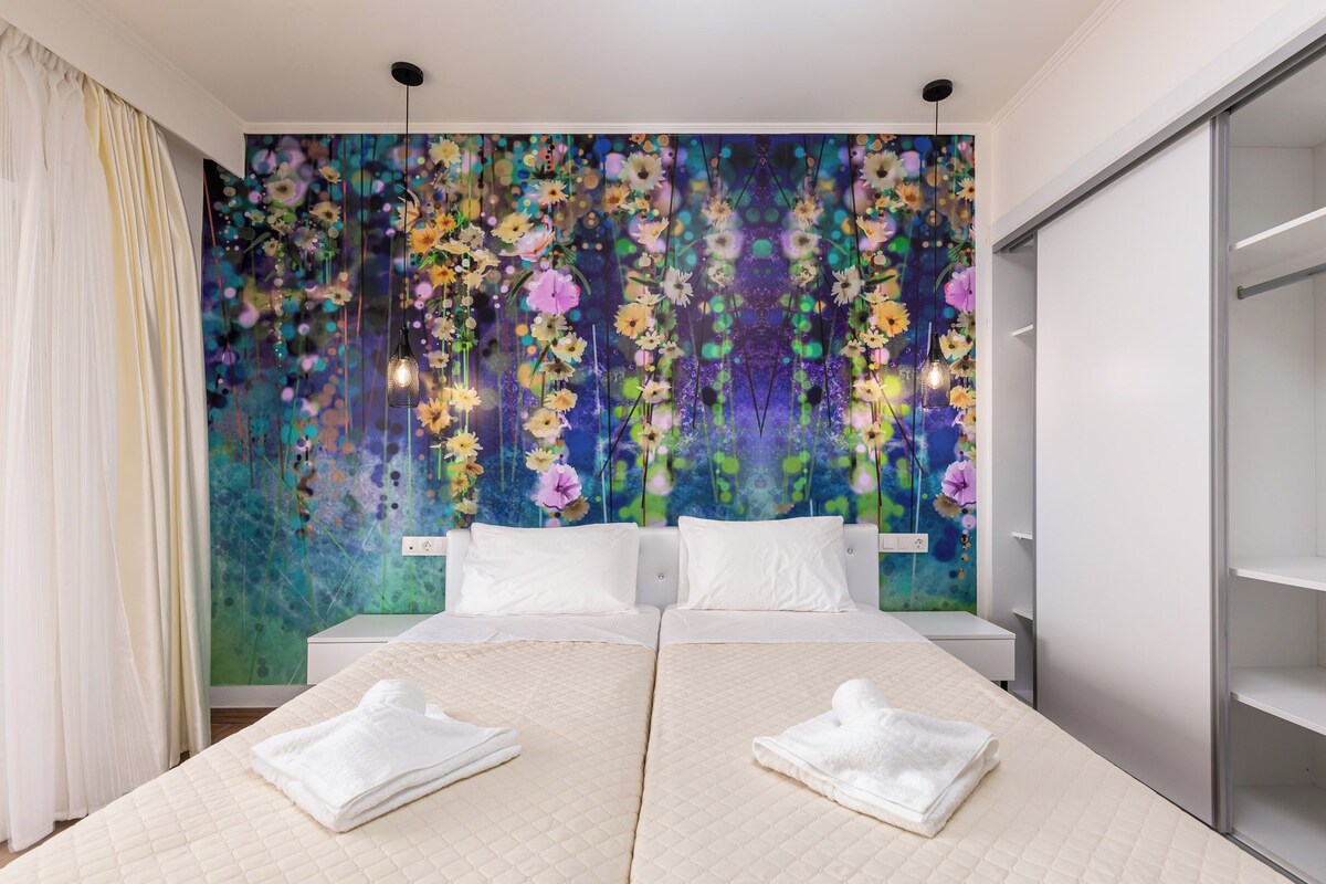 Una cama doble con sábanas blancas, un gran mural floral en la pared y un armario a la derecha.
