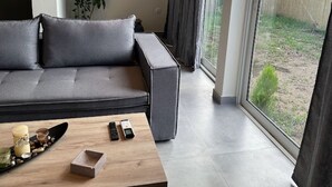 Ein modernes Wohnzimmer mit einem grauen Sofa, einem Holztisch und einem großen Fenster mit Vorhängen.