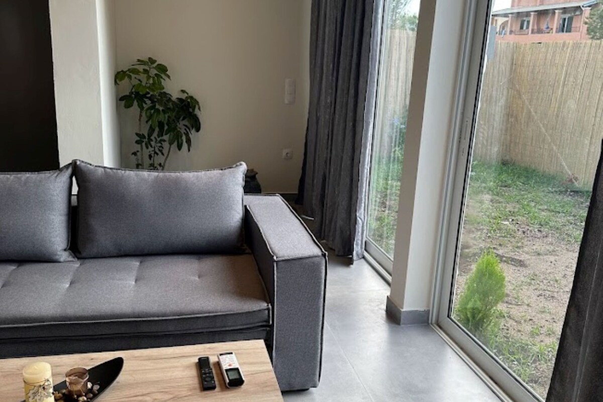 Una sala de estar moderna con un sofá gris, una mesa de centro de madera y un ventanal con cortinas.