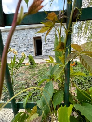 A stone building with a small door, surrounded by greenery and a metal fence. - Aqua Luxury Suites (Corfu)
