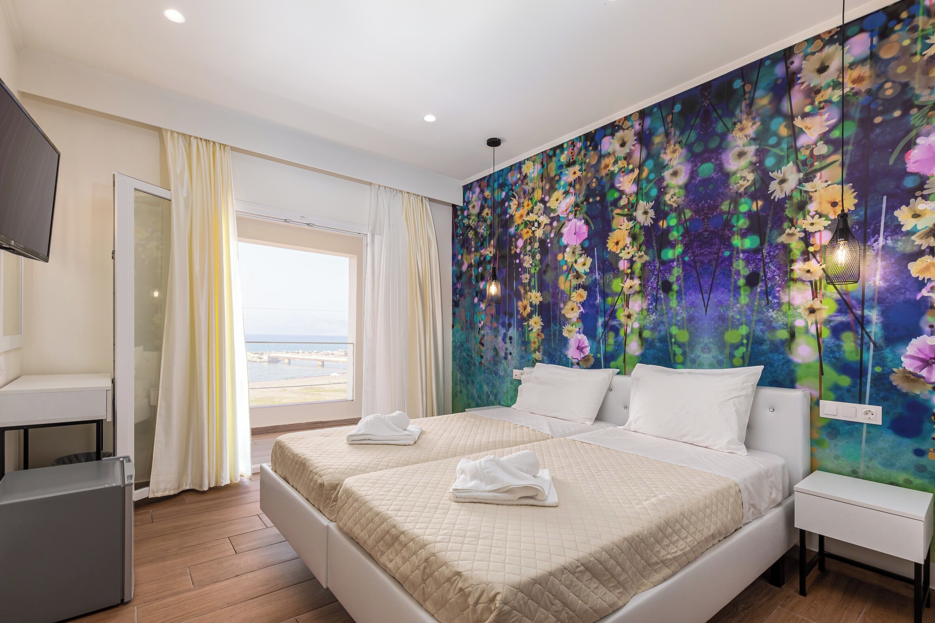 Quarto de hotel com duas camas, televisão, escrivaninha e varanda com vista.