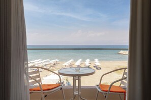 A balcony with two chairs and a table, overlooking a beach with umbrellas and lounge chairs. - Aqua Luxury Suites (Corfu)