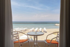Un balcón con dos sillas y una mesa, con vista a una playa con sombrillas y sillas de descanso.