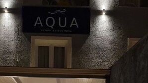 A hotel entrance with a stone facade, a sign reading 'AQUA LUXURY SUITES RODA,' and a welcome sign. - Aqua Luxury Suites (Corfu)