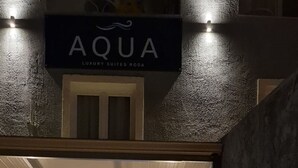 Ein Hotel Eingang mit einer Steinfassade, einer Schilder mit der Aufschrift 'AQUA LUXURY SUITES RODA' und einem Willkommensschild.