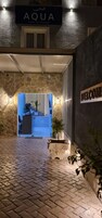 Fachada de hotel de piedra, un letrero que dice 'AQUA LUXURY SUITES RODA' y un cartel de bienvenida.