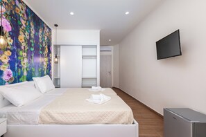 A hotel room with a bed, a flat-screen TV, a wardrobe, and a painting on the wall. - Aqua Luxury Suites (Corfu)