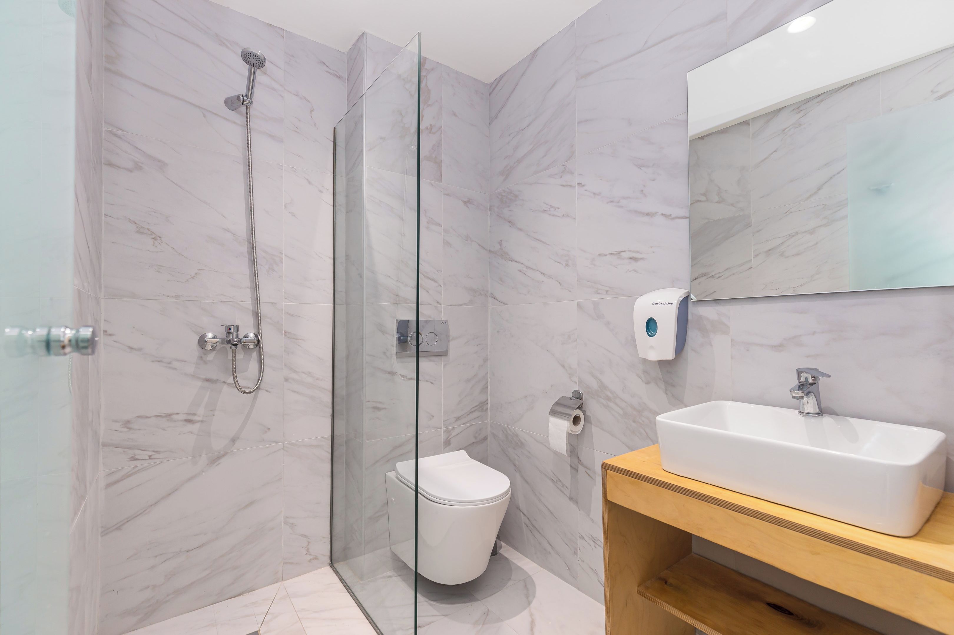 Un baño moderno con ducha envuelta en vidrio, inodoro blanco y tocador de madera con lavamanos.