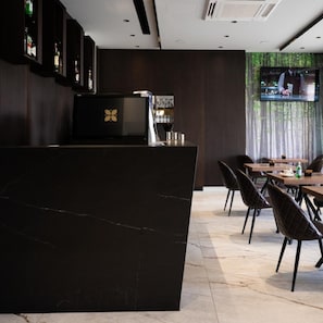 A modern bar area with a black countertop, a TV screen, and a seating area with tables and chairs. - Emery Hotel Pristina (Pristina)