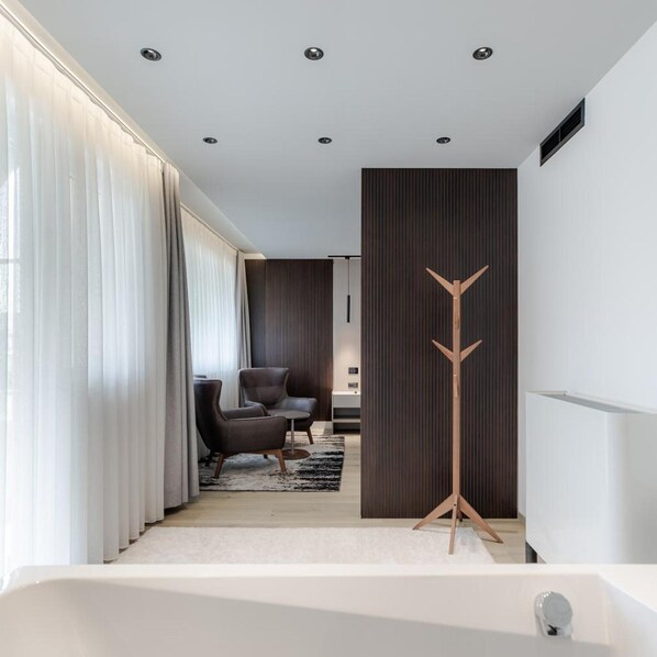 A modern bathroom with a bathtub, a wooden floor, and a seating area with a chair and a small table. - Emery Hotel Pristina (Pristina)