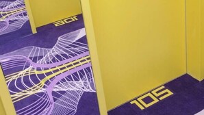 A hallway with yellow lockers and purple carpet with white abstract designs. - Prize by Radisson, Erfurt City (Erfurt)