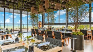 A restaurant with tables set for dining, large windows, and hanging plants. - Bara Hotel Joao Pessoa (João Pessoa)