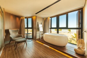Een moderne badkamer met een groot bad, een stoel en uitzicht op het strand.