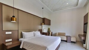 A modern hotel room with a large bed, bedside tables, a seating area, and a ceiling with a unique design. - Accord Chrome Airport Hotel (Chennai)