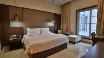 A hotel room with a large bed, bedside tables, a desk, and a window with curtains.