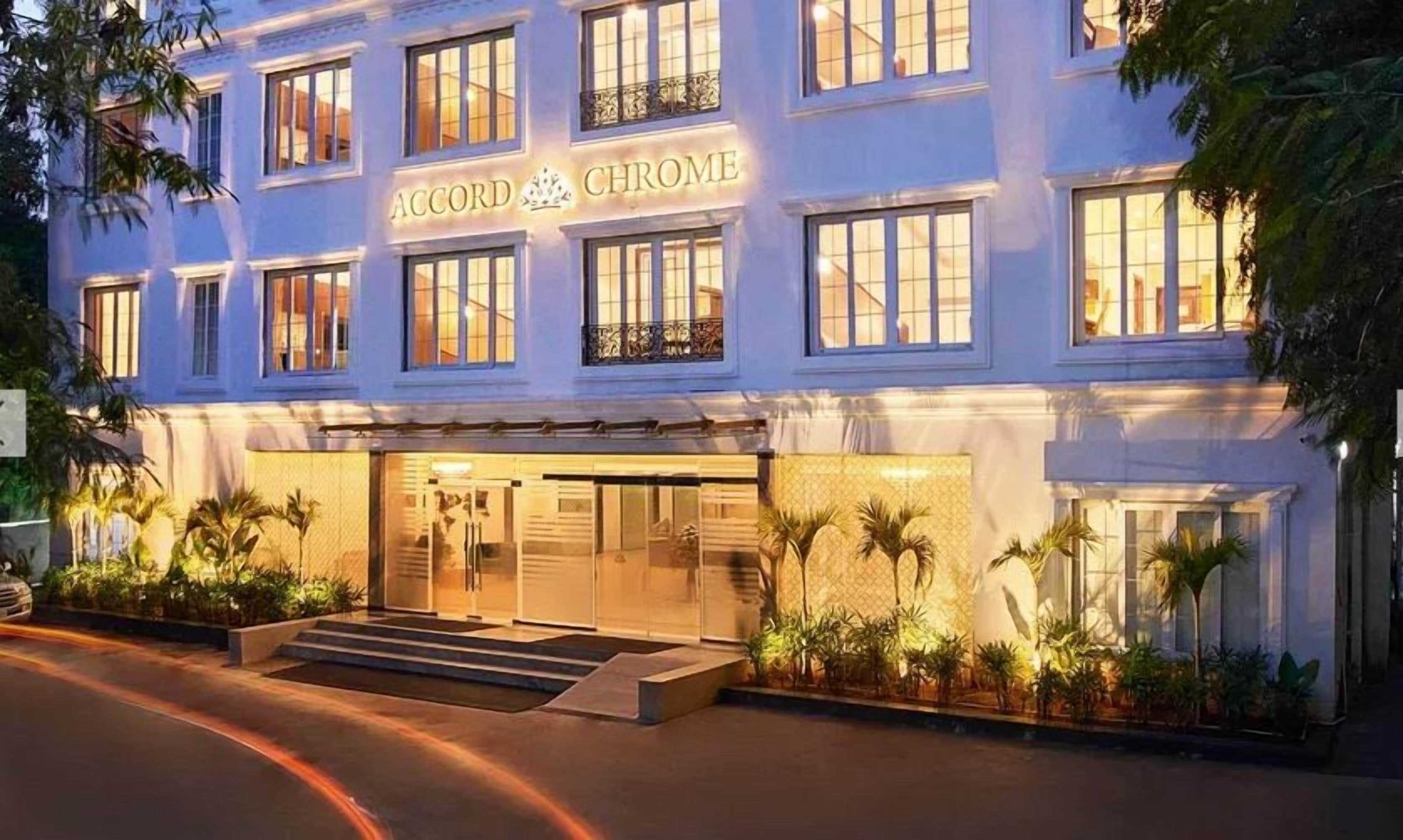 A hotel with a sign reading 'Accord & Chrome,' featuring a modern facade, a well-lit entrance, and a landscaped front garden.