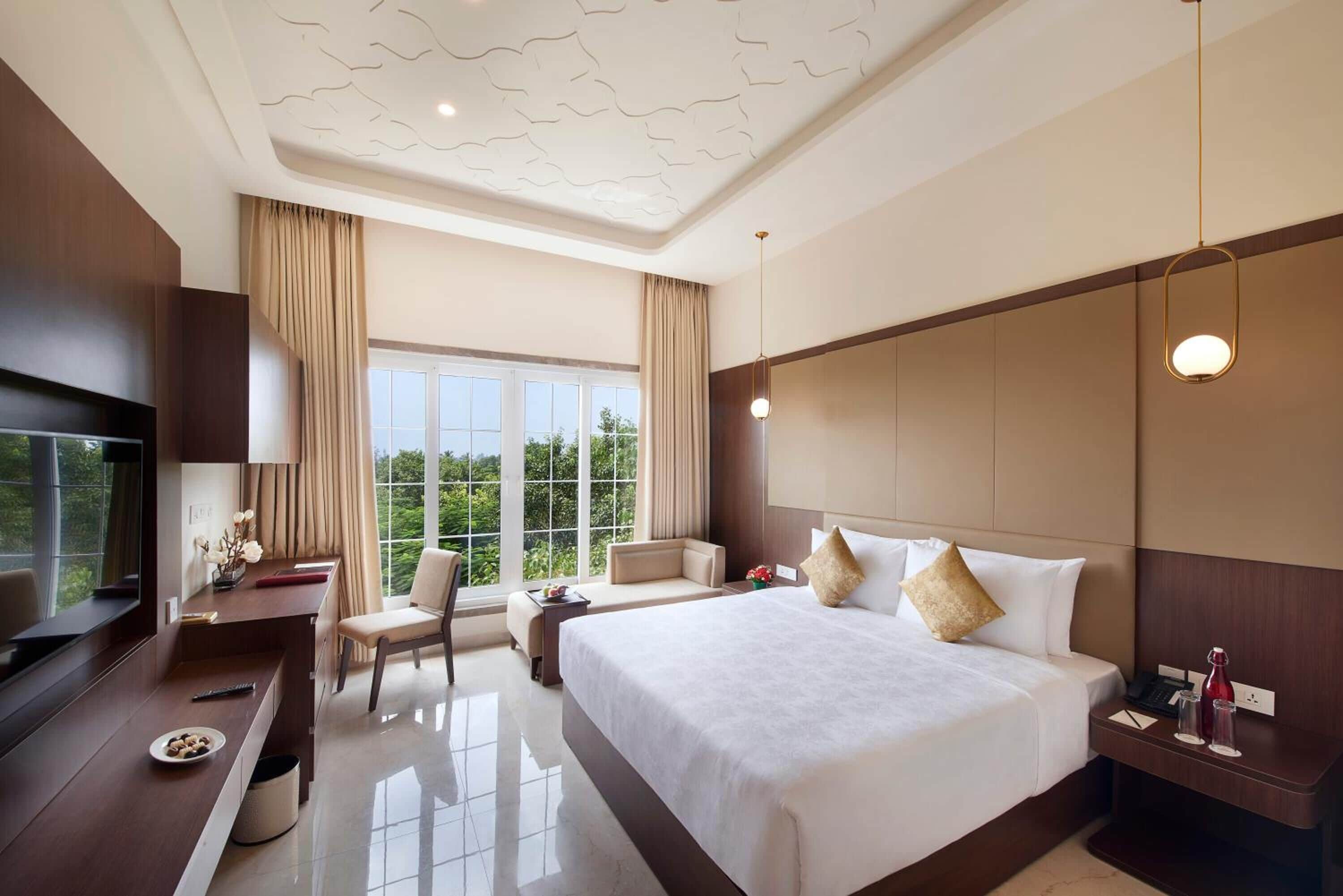 A modern hotel room with a large bed, a desk, a TV, and a view of the outdoors.