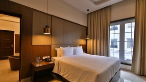 A hotel room with a large bed, a nightstand with a phone and water bottles, a wall-mounted lamp, and a view of the outside through a window with curtains. - Accord Chrome Airport Hotel (Chennai)