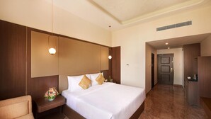 A hotel room with a large bed, a bedside table with a vase of flowers, a chair, and a wardrobe. - Accord Chrome Airport Hotel (Chennai)