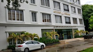 A white building with the sign "Accord Chrome" on the facade. There are palm trees in front, and a white car parked on the street. - Accord Chrome Airport Hotel (Chennai)