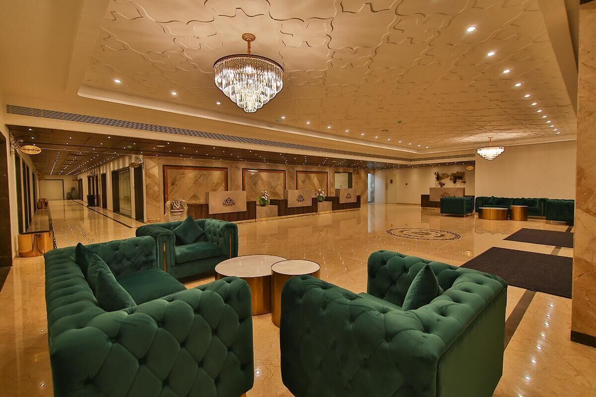 Um hall amplo com sofás estofados em verde, um candelabro e piso de mármore.