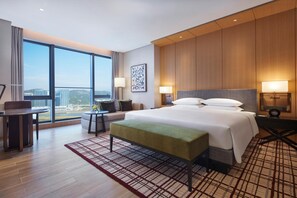 A hotel room with a large bed, a desk, a chair, a window with a city view, and a wall-mounted artwork. - Hyatt Regency Hengqin (Zhuhai)