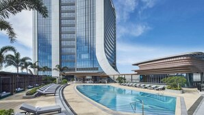 Un hotel modern amb façana de vidre corbat, zona de piscina amb gandules i palmeres.