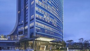 Un hotel modern amb una façana corba, diverses plantes i una entrada destacada amb zona coberta.