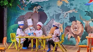 Un grup de persones amb uniforme de cuiners assegudes al voltant d'una taula en una sala amb un mural d'animals de la selva.