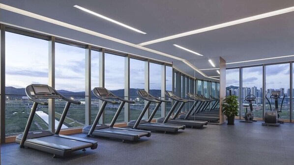 A modern gym with treadmills and exercise equipment, large windows offering a city view. - Hyatt Regency Hengqin (Zhuhai)