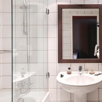 A bathroom with a glass shower enclosure, a white sink, and a mirror with a wooden frame.