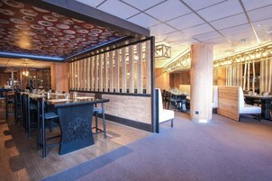 A modern restaurant interior with wooden paneling, a patterned ceiling, and a mix of seating arrangements.