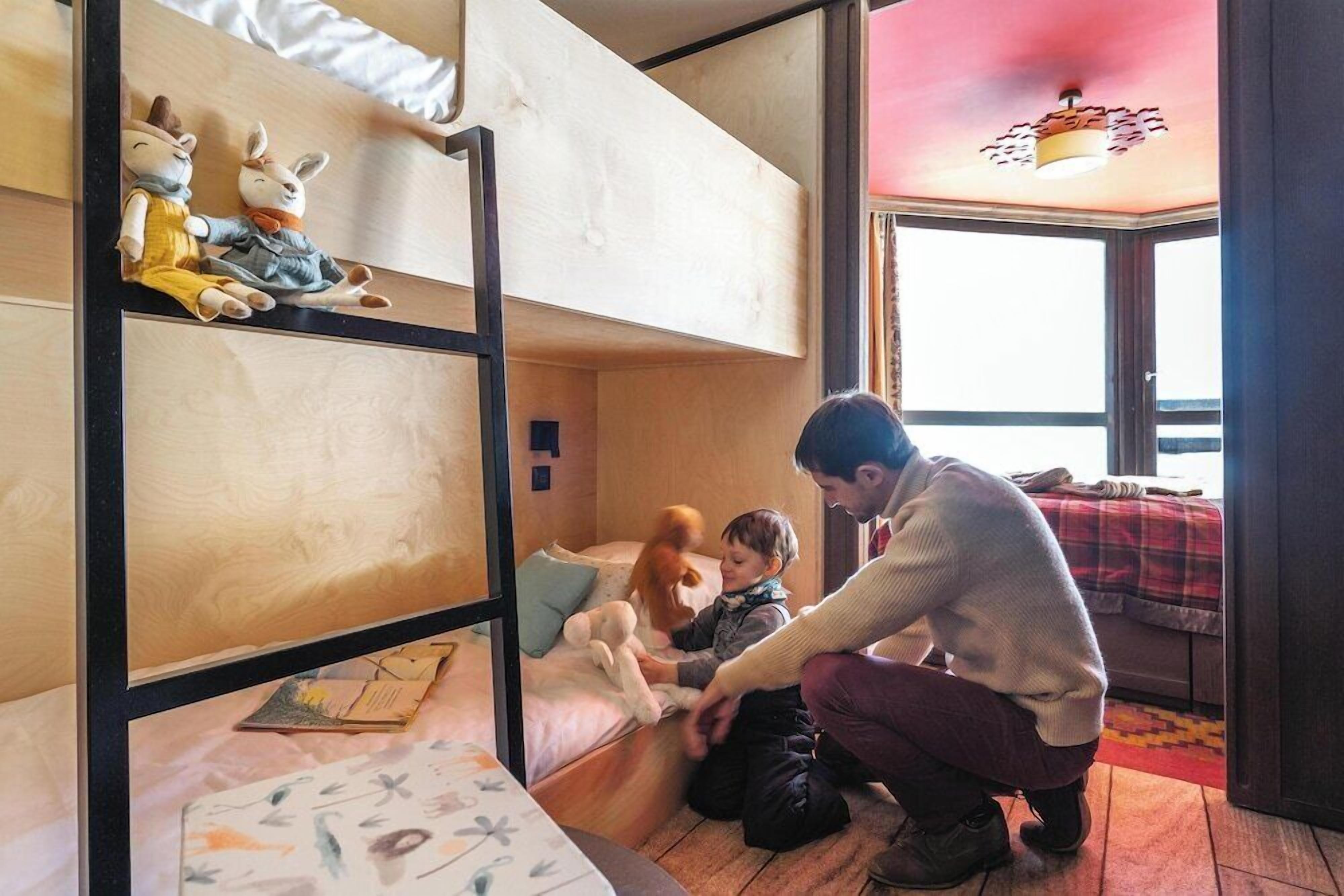 Een slaapkamer met een stapelbed, waarin een kind en volwassene samenspelen.