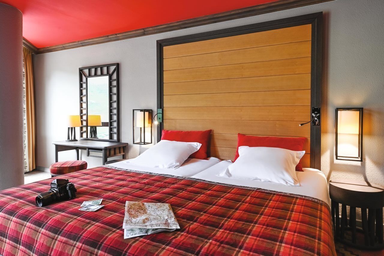 A hotel room with a large bed, a wooden headboard, a desk with a lamp, and a mirror.