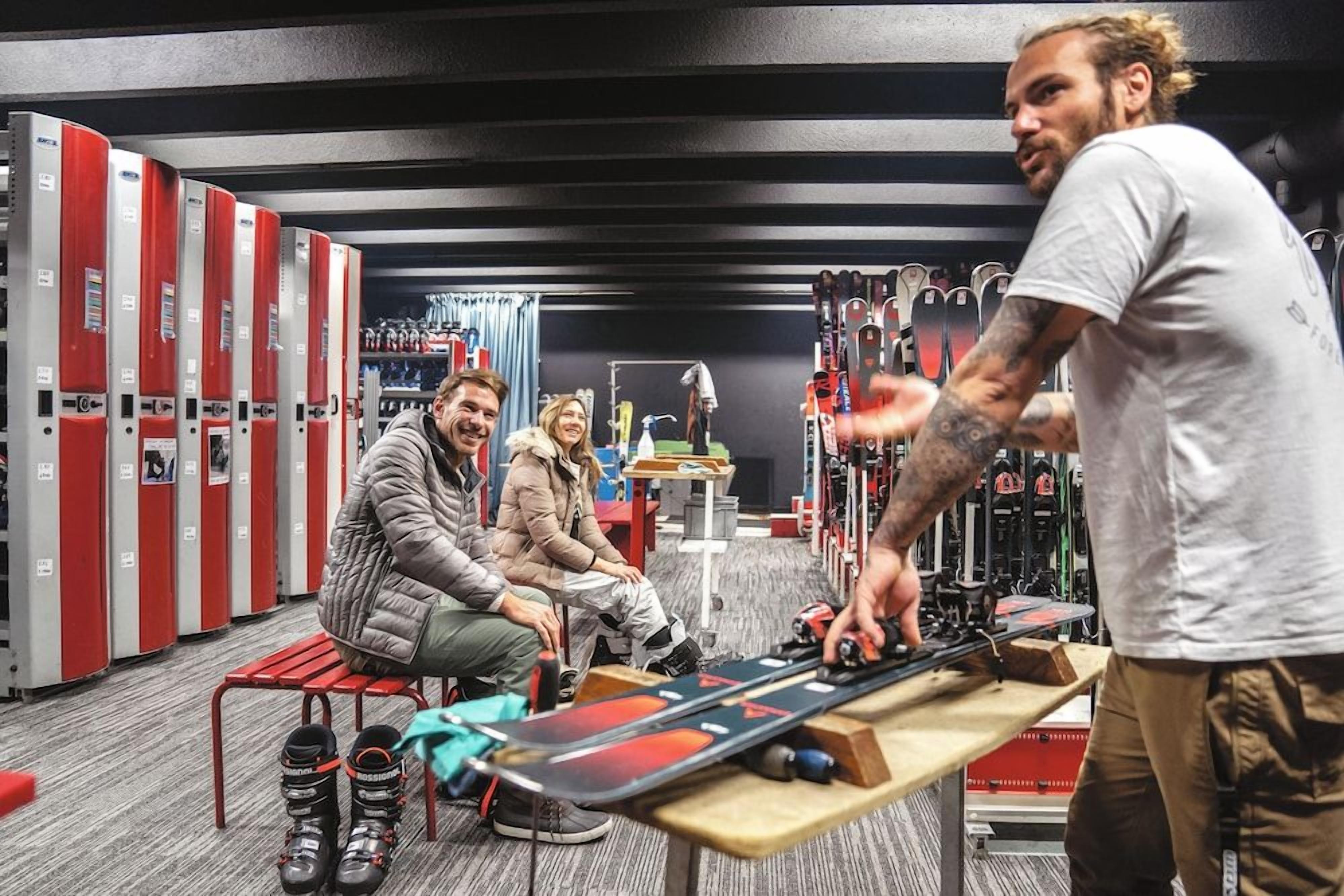A ski equipment room with benches, ski racks, and a table with ski boots.