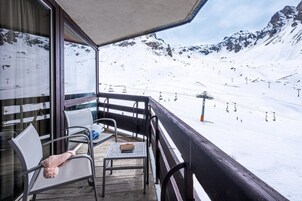A balcony with a view of a snowy mountain slope and ski lifts.