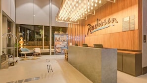 A modern reception area with a wooden reception desk, a seating area with chairs, and a large illuminated sign. - Radisson Hotel Pinheiros, Sao Paulo (São Paulo)