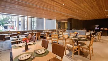Um restaurante moderno com painéis de teto em madeira, janelas amplas e diversas opções de assentos, incluindo mesas e cabines.