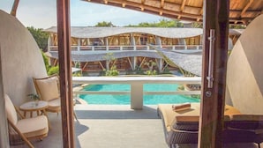 A poolside area with lounge chairs and a view of a building with a wooden roof and a swimming pool. - Pearl Sunset Resort (Gili Trawangan)