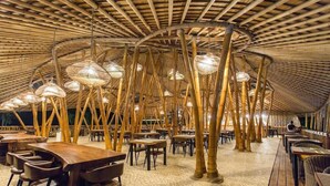 An indoor dining area with bamboo ceiling structures and hanging light fixtures. Tables and chairs are arranged for seating. - Pearl Sunset Resort (Gili Trawangan)