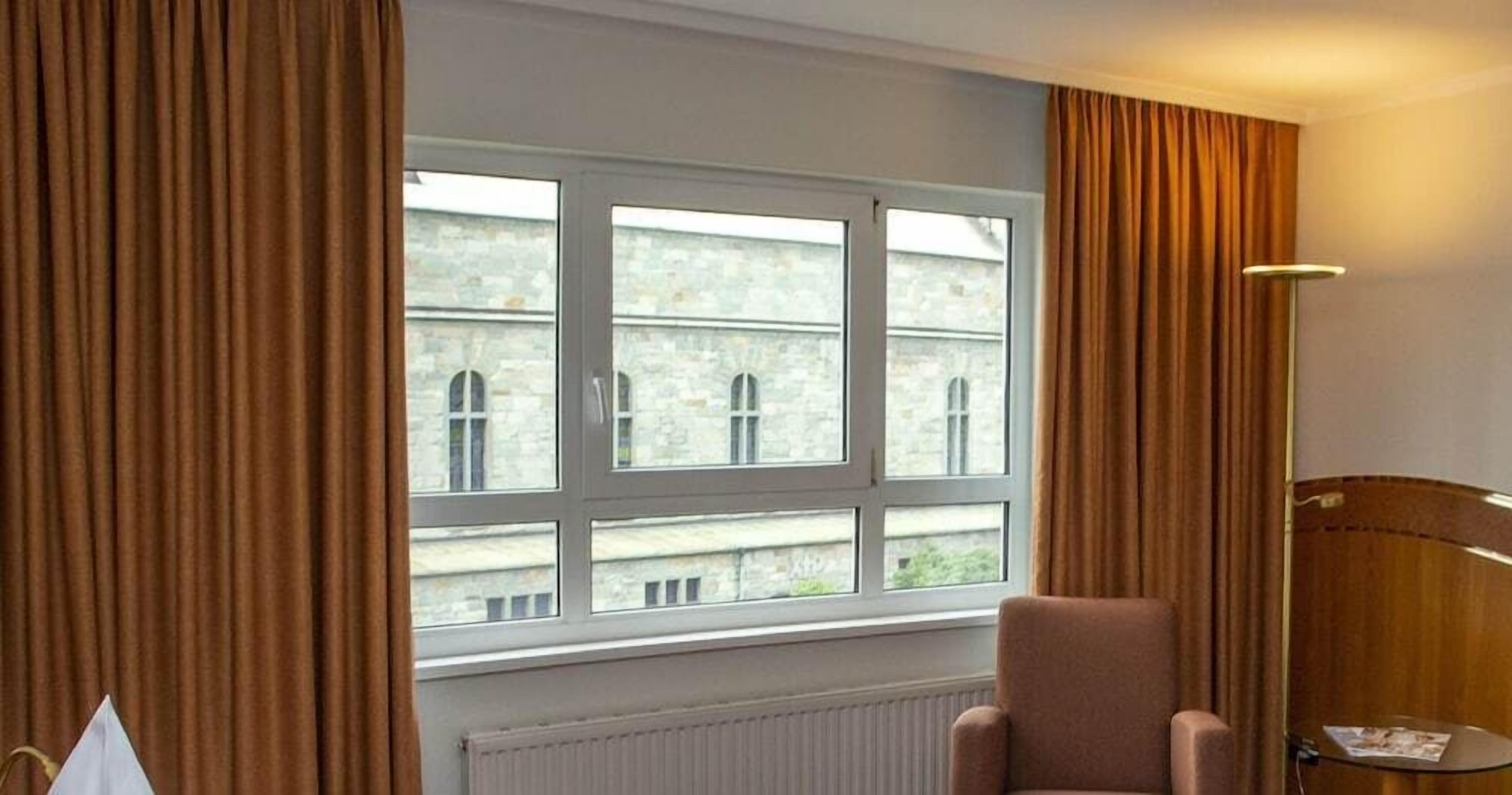 Ein Zimmer mit großem Fenster, Heizkörper, Stuhl und Lampe.