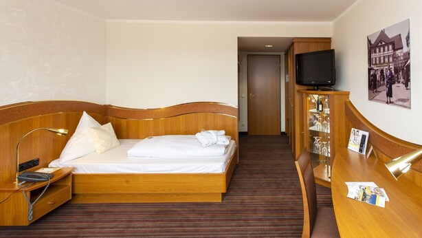 Una camera d'albergo con un letto in legno, una scrivania con il telefono, un televisore e un minibar.